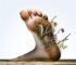 alt_text: A close-up of a foot's heel entwined with thorns and natural elements, symbolizing pain and beauty.